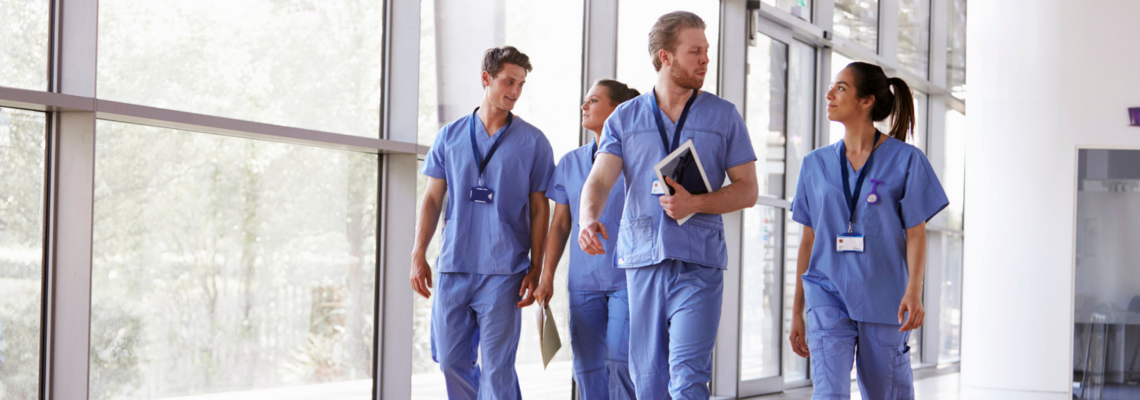 Abbildung vier Krankenpfleger gehen nebeneinander einen Gang entlang 