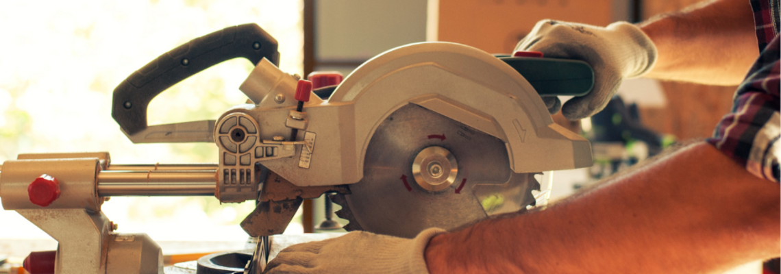 Abbildung Mann mit Schutzbrille sägt mit einer Sägemaschine ein Holzbrett durch